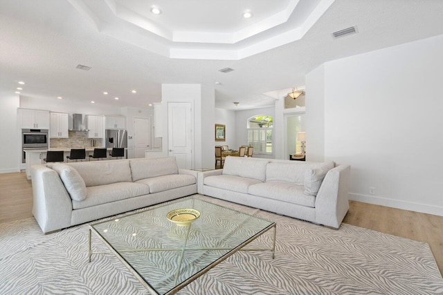 living room with a textured ceiling, light wood-type flooring, and a tray ceiling