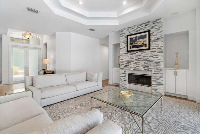 living room featuring a tray ceiling, french doors, a tile fireplace, and light hardwood / wood-style flooring