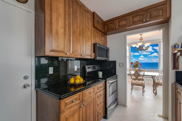 kitchen with light tile patterned floors, appliances with stainless steel finishes, backsplash, dark stone counters, and a notable chandelier