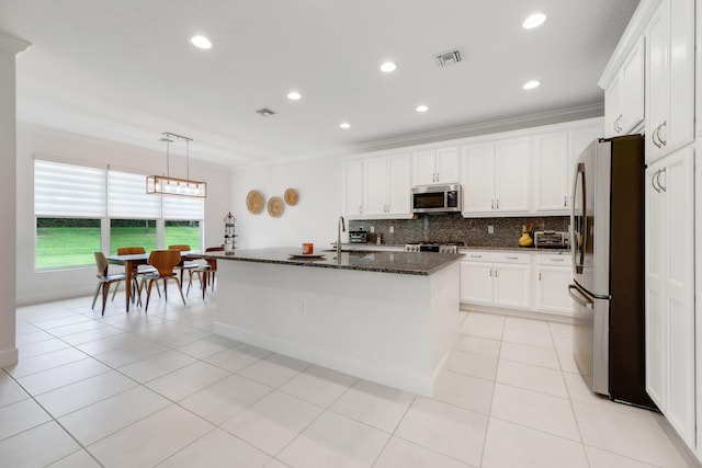 kitchen with a center island with sink, backsplash, appliances with stainless steel finishes, white cabinets, and dark stone countertops