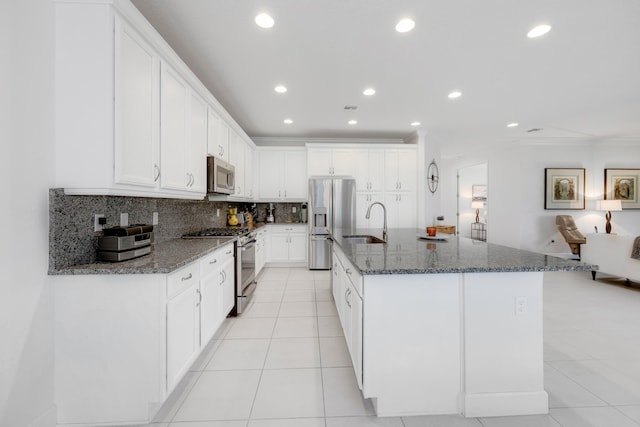 kitchen with stainless steel appliances, dark stone countertops, white cabinets, and a center island with sink