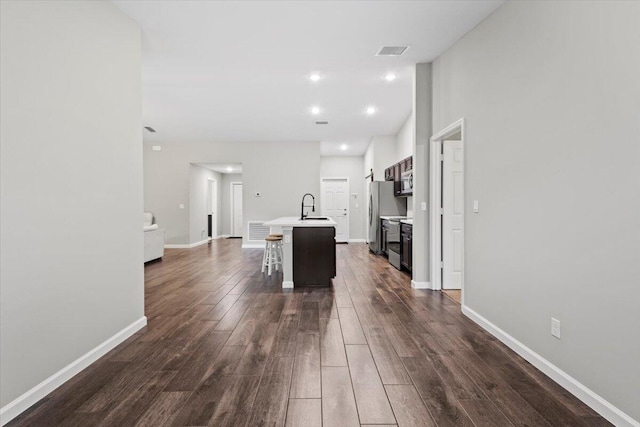 kitchen with appliances with stainless steel finishes, sink, an island with sink, dark wood-type flooring, and a breakfast bar