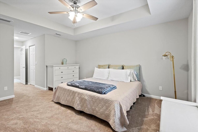 bedroom with light carpet, a tray ceiling, and ceiling fan