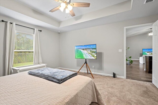 carpeted bedroom with ceiling fan and a tray ceiling