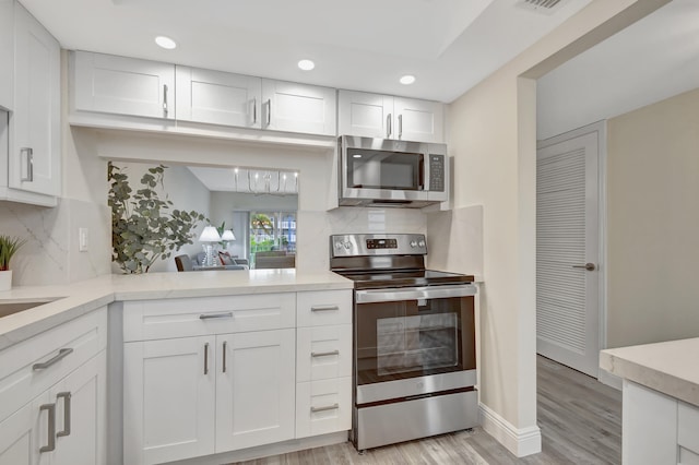 kitchen featuring backsplash, white cabinets, light wood-type flooring, and appliances with stainless steel finishes