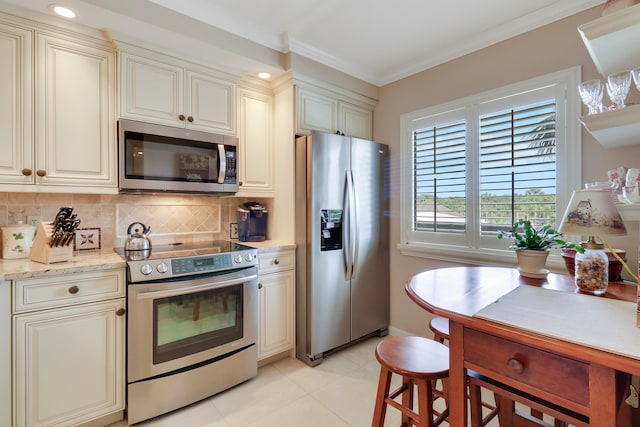 kitchen featuring light tile patterned flooring, cream cabinetry, appliances with stainless steel finishes, and ornamental molding