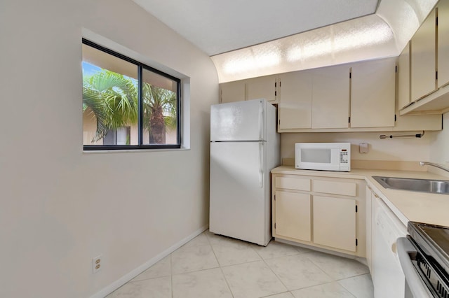 kitchen featuring light tile patterned floors, cream cabinetry, sink, and white appliances