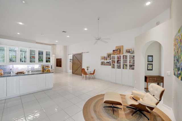 interior space with tasteful backsplash, a barn door, ceiling fan, white cabinets, and light tile patterned floors