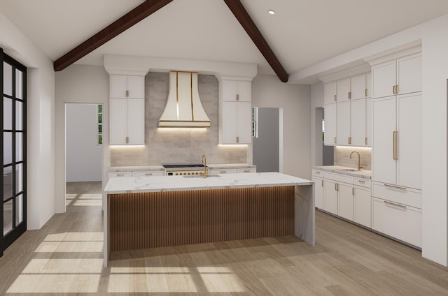 kitchen featuring sink, premium range hood, white cabinets, and a center island with sink