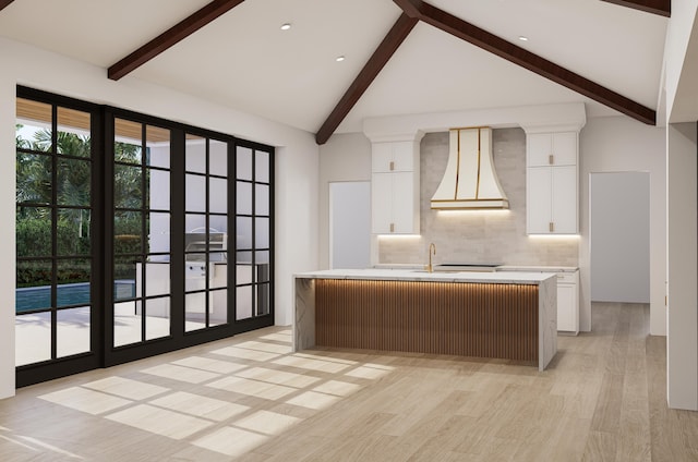 kitchen featuring light hardwood / wood-style floors, premium range hood, white cabinetry, beam ceiling, and a center island with sink