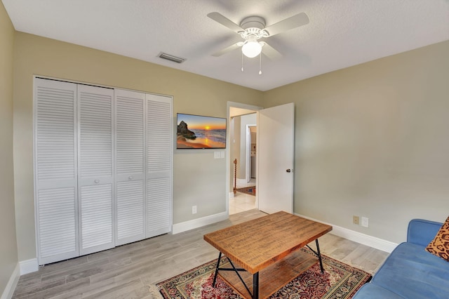 living room with ceiling fan, light wood-type flooring, and a textured ceiling