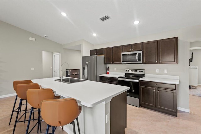 kitchen featuring appliances with stainless steel finishes, sink, an island with sink, a kitchen breakfast bar, and vaulted ceiling