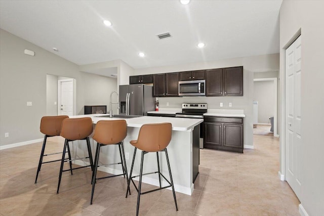 kitchen with appliances with stainless steel finishes, sink, vaulted ceiling, a breakfast bar area, and a kitchen island with sink