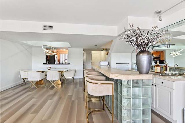 bar featuring stainless steel refrigerator with ice dispenser, sink, hardwood / wood-style floors, decorative light fixtures, and white cabinetry