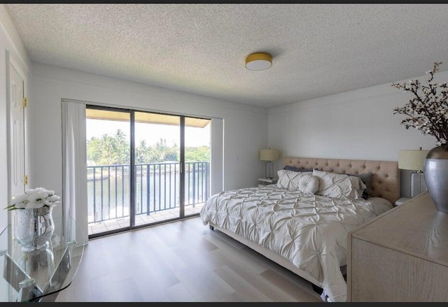 bedroom featuring a water view, access to exterior, and a textured ceiling