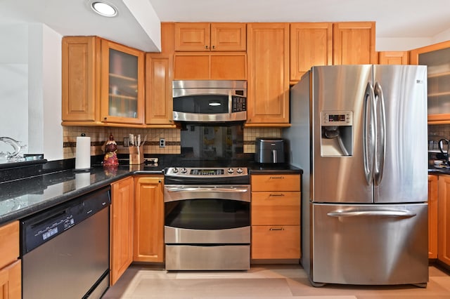 kitchen featuring decorative backsplash, appliances with stainless steel finishes, and dark stone counters