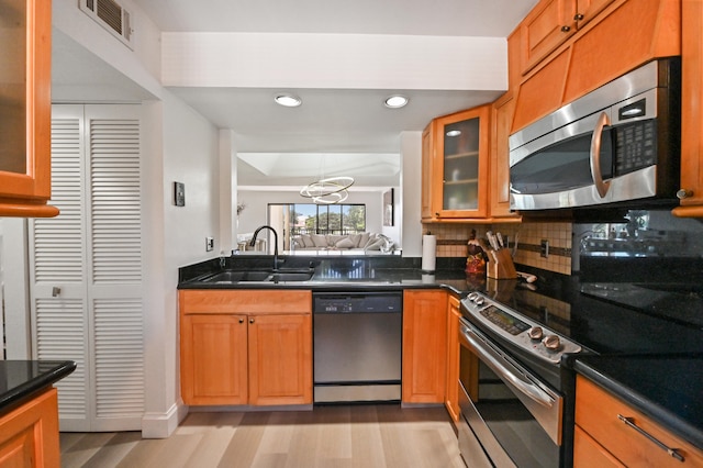 kitchen featuring decorative backsplash, appliances with stainless steel finishes, light hardwood / wood-style flooring, a notable chandelier, and sink