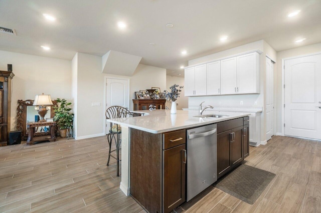 kitchen featuring sink, stainless steel dishwasher, white cabinets, light hardwood / wood-style flooring, and a center island with sink