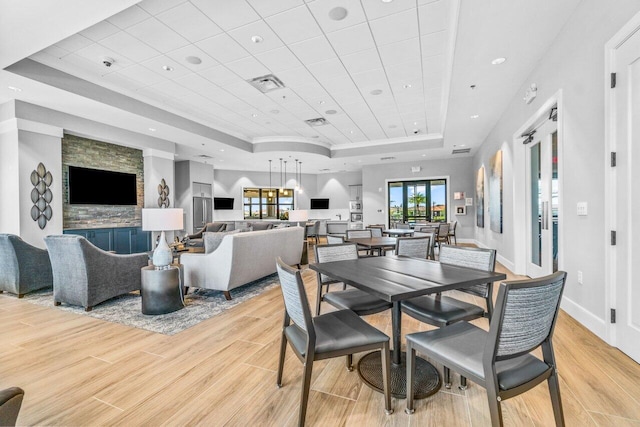 dining area featuring a tray ceiling, light wood-type flooring, and a fireplace