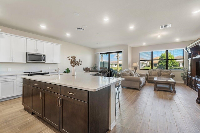 kitchen with a center island with sink, a breakfast bar, white cabinetry, and light wood-type flooring