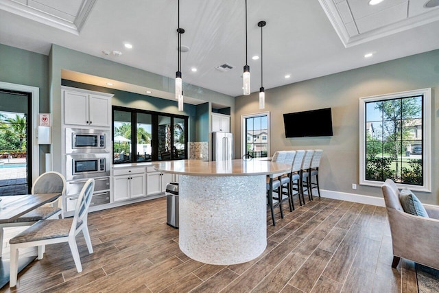 kitchen with white cabinets, hanging light fixtures, a breakfast bar area, a kitchen island, and light hardwood / wood-style flooring