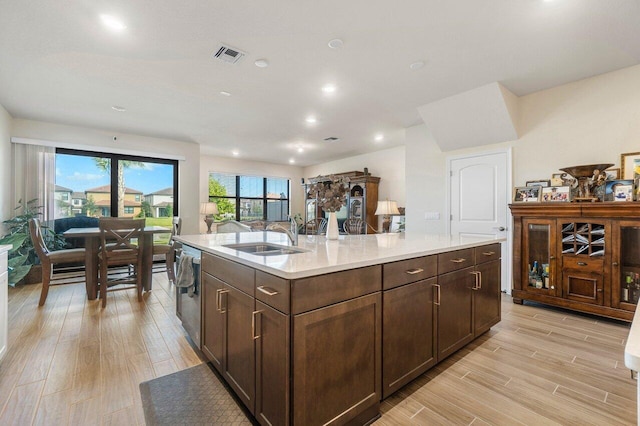 kitchen featuring light wood-type flooring, stainless steel dishwasher, sink, and an island with sink