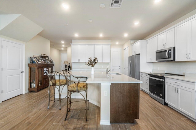 kitchen featuring a kitchen breakfast bar, white cabinetry, light hardwood / wood-style floors, stainless steel appliances, and a center island with sink