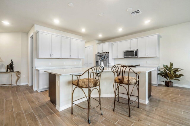 kitchen with white cabinets, a kitchen island with sink, a kitchen bar, light hardwood / wood-style flooring, and stainless steel appliances