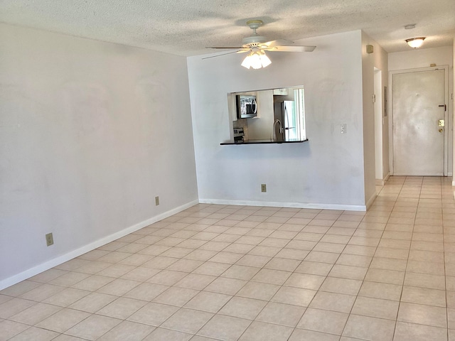 spare room with a textured ceiling, light tile patterned floors, and ceiling fan