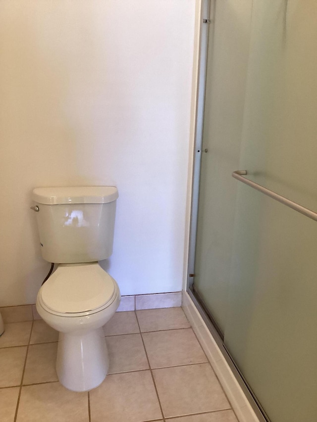 bathroom with tile patterned floors, toilet, and a shower with door