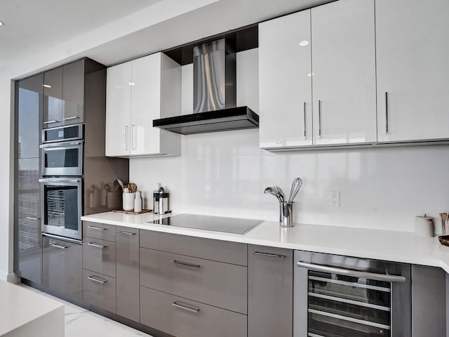 kitchen featuring wall chimney range hood, black electric cooktop, stainless steel double oven, gray cabinets, and wine cooler