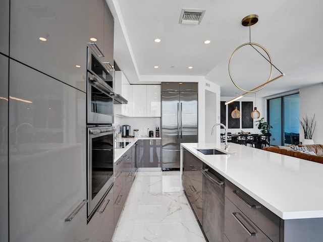 kitchen with appliances with stainless steel finishes, sink, an island with sink, decorative light fixtures, and white cabinets