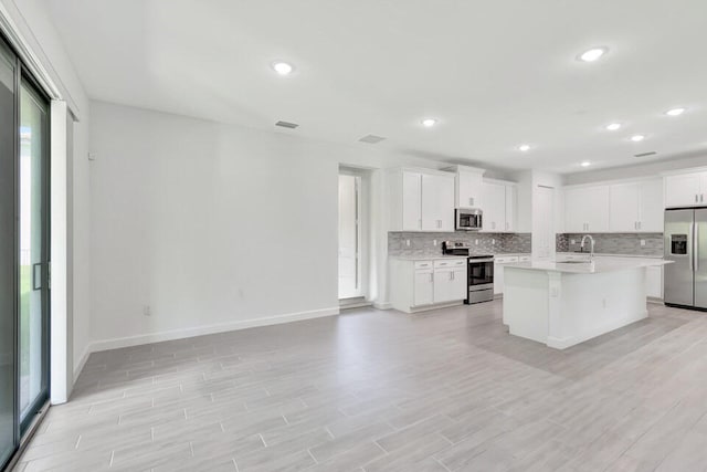 kitchen with backsplash, stainless steel appliances, a center island, light hardwood / wood-style floors, and white cabinetry