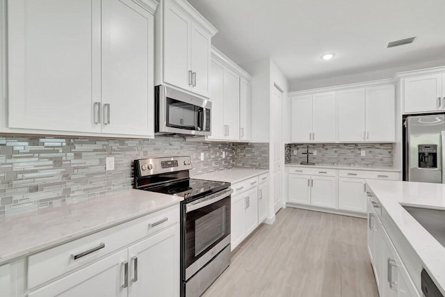 kitchen featuring decorative backsplash, white cabinetry, appliances with stainless steel finishes, and light hardwood / wood-style flooring