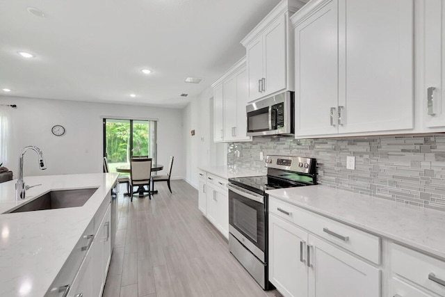 kitchen featuring light stone countertops, white cabinetry, sink, light hardwood / wood-style flooring, and appliances with stainless steel finishes