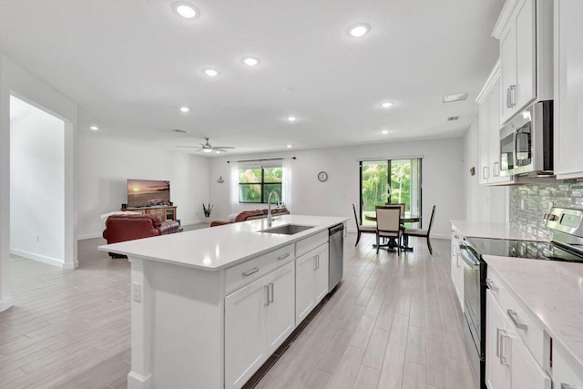 kitchen with white cabinetry, sink, stainless steel appliances, a kitchen island with sink, and light wood-type flooring