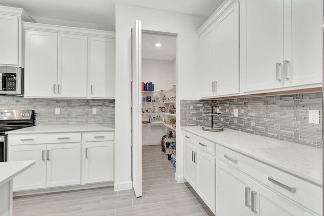 kitchen featuring light stone countertops, backsplash, stainless steel appliances, and white cabinetry