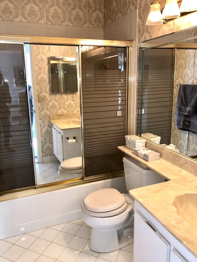 bathroom with tile patterned flooring, toilet, vanity, combined bath / shower with glass door, and wallpapered walls