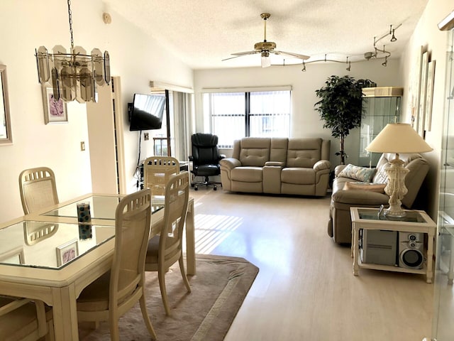 dining room featuring ceiling fan with notable chandelier, light hardwood / wood-style flooring, a textured ceiling, and vaulted ceiling