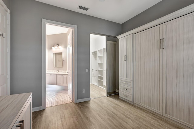 unfurnished bedroom with connected bathroom, a closet, a spacious closet, and light hardwood / wood-style floors