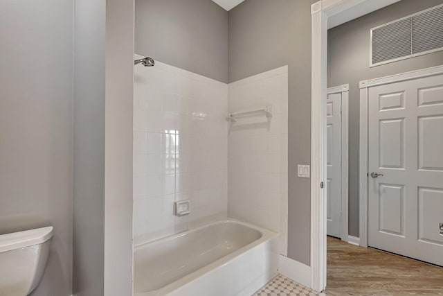 bathroom with hardwood / wood-style floors, tiled shower / bath, and toilet