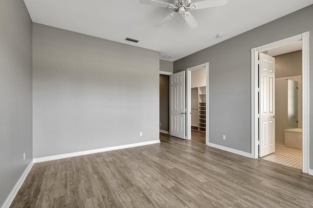 unfurnished bedroom featuring light hardwood / wood-style floors, ceiling fan, a spacious closet, connected bathroom, and a closet