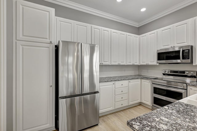 kitchen featuring stainless steel appliances, white cabinets, dark stone counters, and ornamental molding