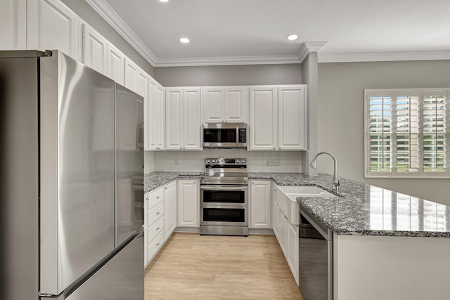 kitchen with white cabinetry, kitchen peninsula, stainless steel appliances, and dark stone counters