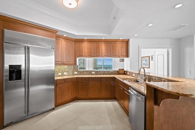 kitchen featuring kitchen peninsula, light stone countertops, backsplash, stainless steel appliances, and crown molding