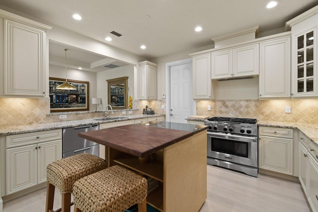 kitchen featuring sink, appliances with stainless steel finishes, butcher block counters, a kitchen breakfast bar, and decorative light fixtures