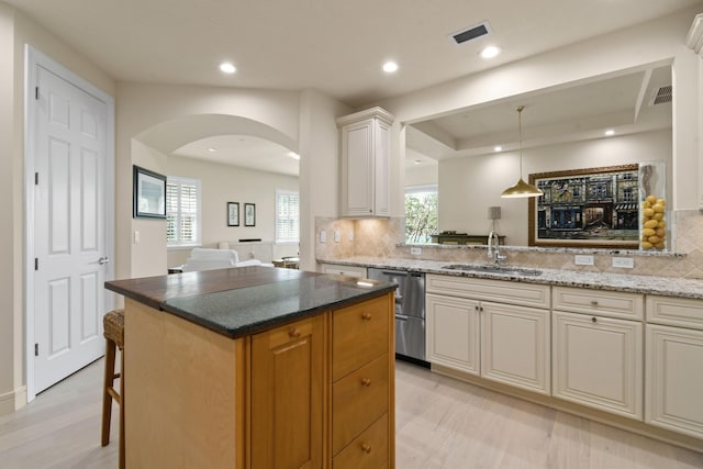 kitchen with a kitchen island, tasteful backsplash, dishwasher, sink, and light stone countertops