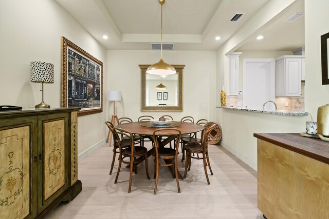 dining area with a tray ceiling and light hardwood / wood-style flooring