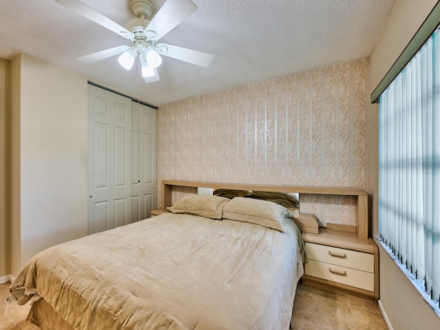 bedroom featuring light tile patterned flooring, ceiling fan, a textured ceiling, and a closet