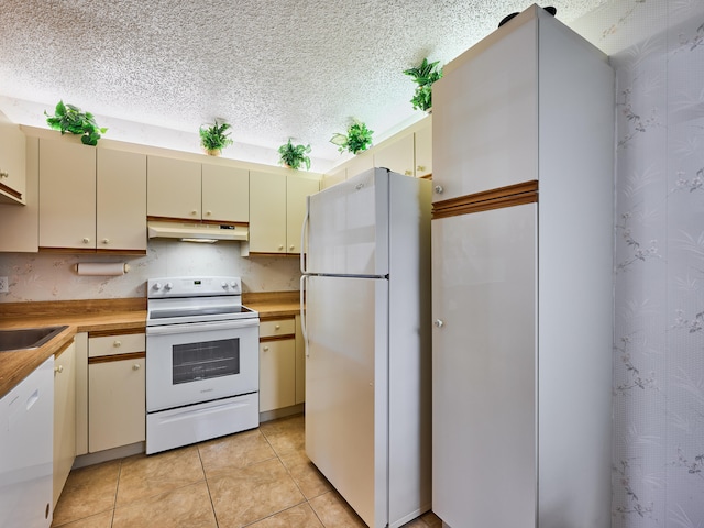 kitchen featuring cream cabinets, a textured ceiling, white appliances, and light tile patterned floors